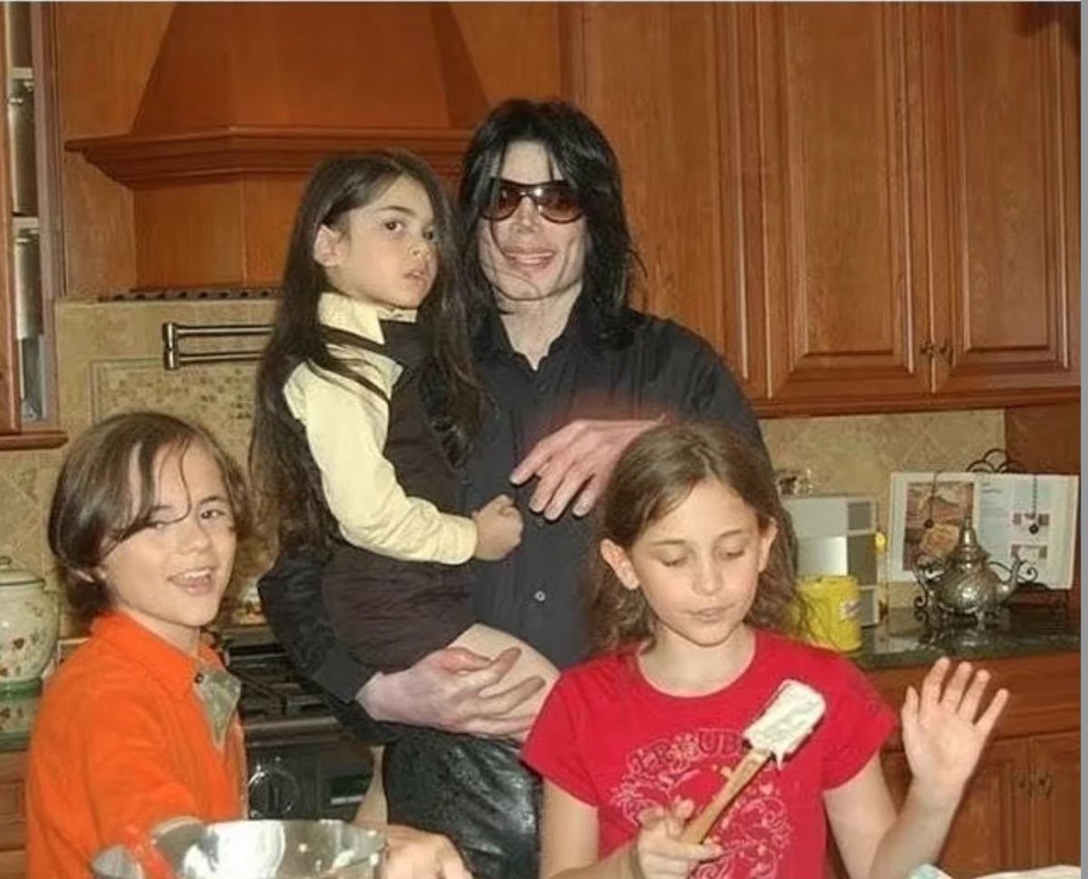 Michael Jackson at home in the kitchen with his three children — Prince, Paris and Blanket — baking together. A private, ordinary, loving family moment.